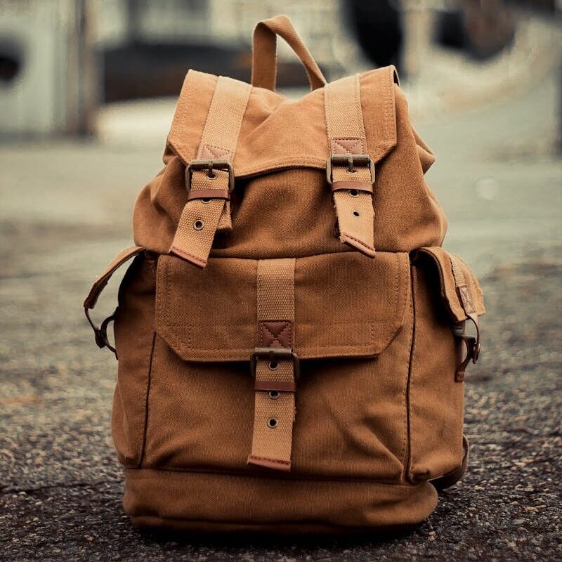 Voor wie? Close-up of a brown backpack on a blurred urban street background.